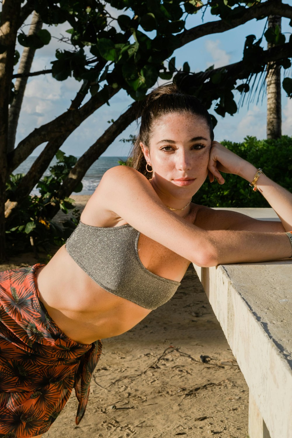 woman in gray crop top and orange and black floral skirt sitting on gray concrete bench