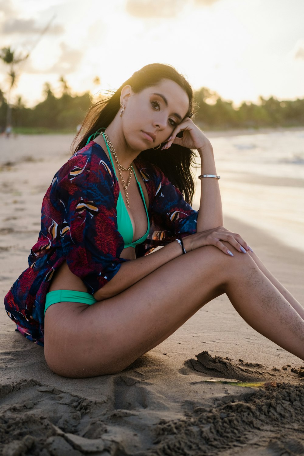 woman in red and blue floral dress sitting on brown sand during daytime