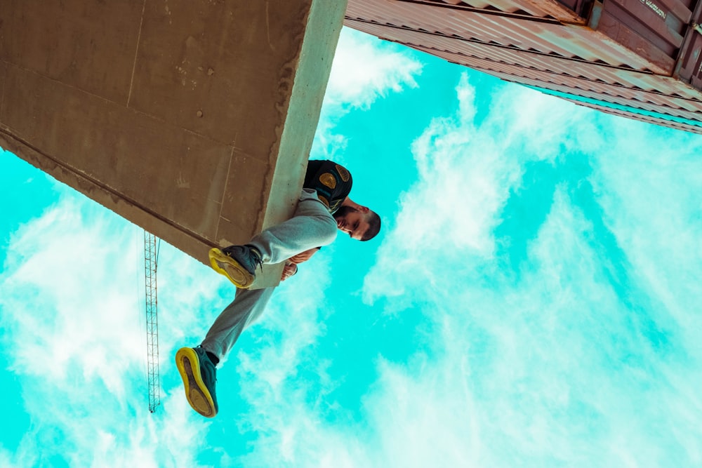 Homme en T-shirt bleu et pantalon blanc debout sur un sol en béton gris sous un ciel bleu