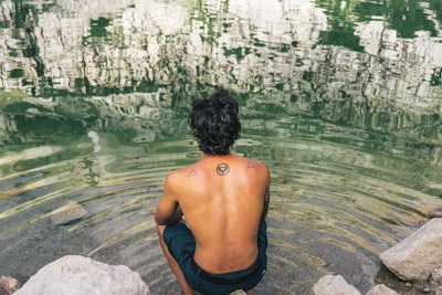 man in black shorts sitting on rock near body of water during daytime back google meet background