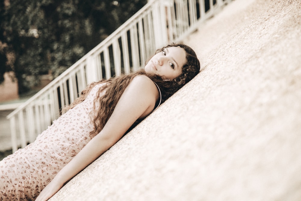 woman in white and pink floral sleeveless dress lying on white sand during daytime