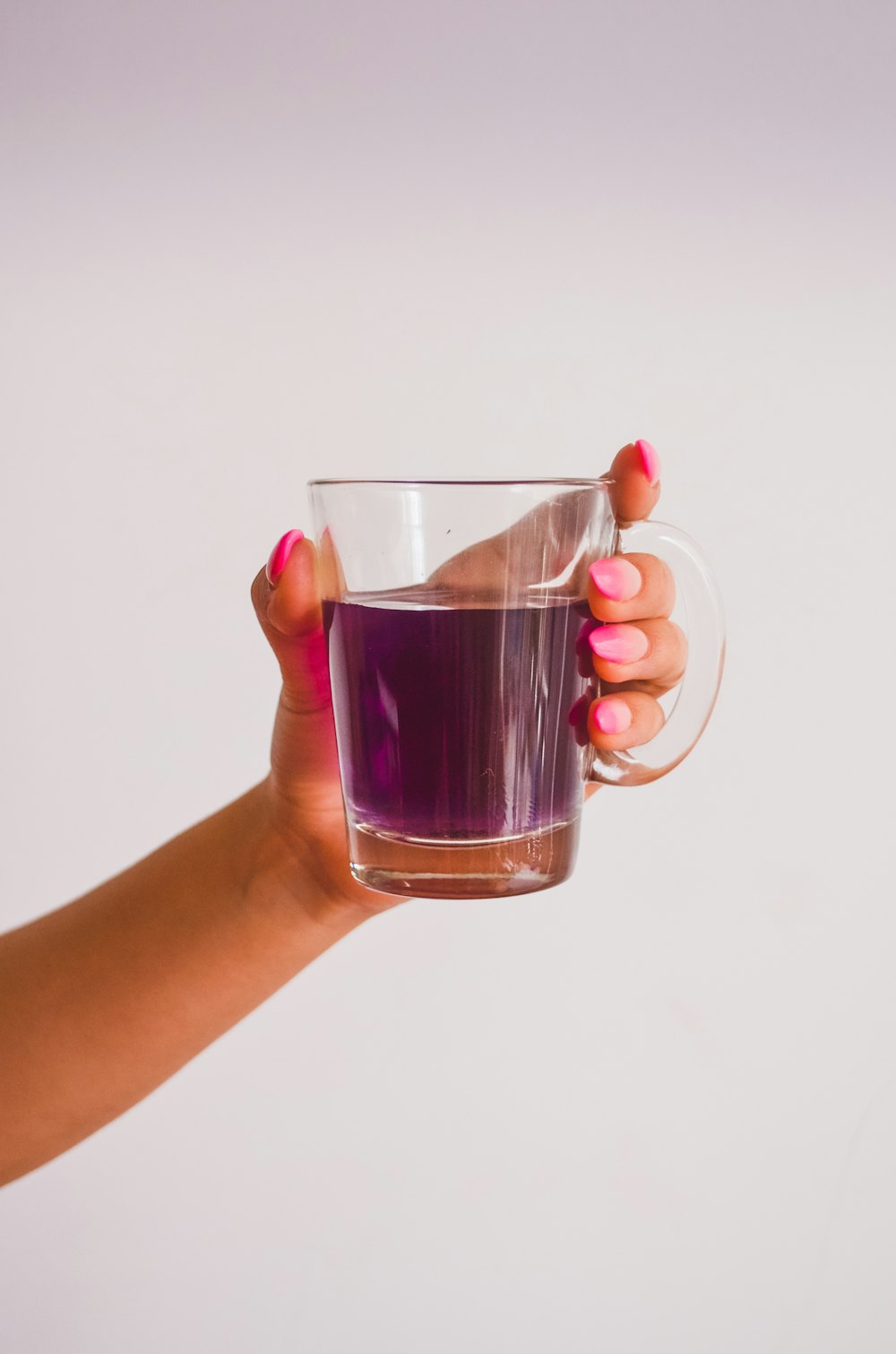 Persona sosteniendo una taza de vidrio transparente con líquido marrón