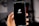 A hand holding a smartphone displaying the TikTok logo against a dark screen, with a blurred background. The hand is positioned prominently in the foreground, and the logo is centered on the phone's display.