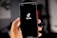 A hand holding a smartphone displaying the TikTok logo against a dark screen, with a blurred background. The hand is positioned prominently in the foreground, and the logo is centered on the phone's display.