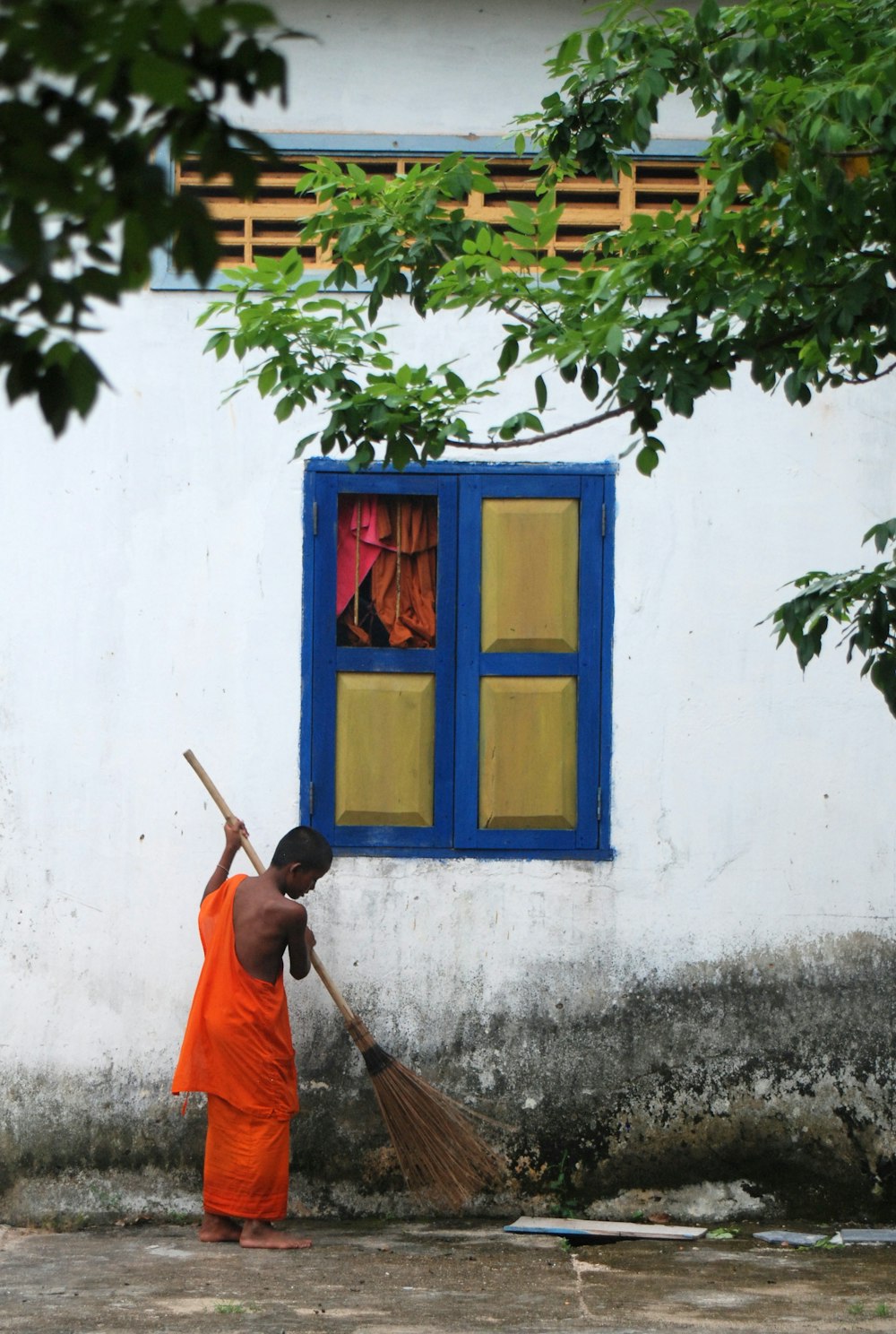 Mann in orangefarbener Robe sitzt neben blauem Holzfenster