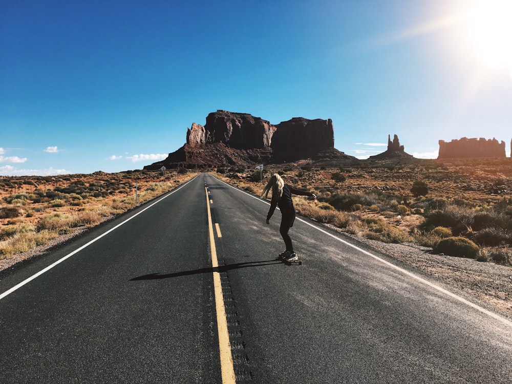 Hombre con chaqueta negra y pantalones negros corriendo en carretera de asfalto gris durante el día