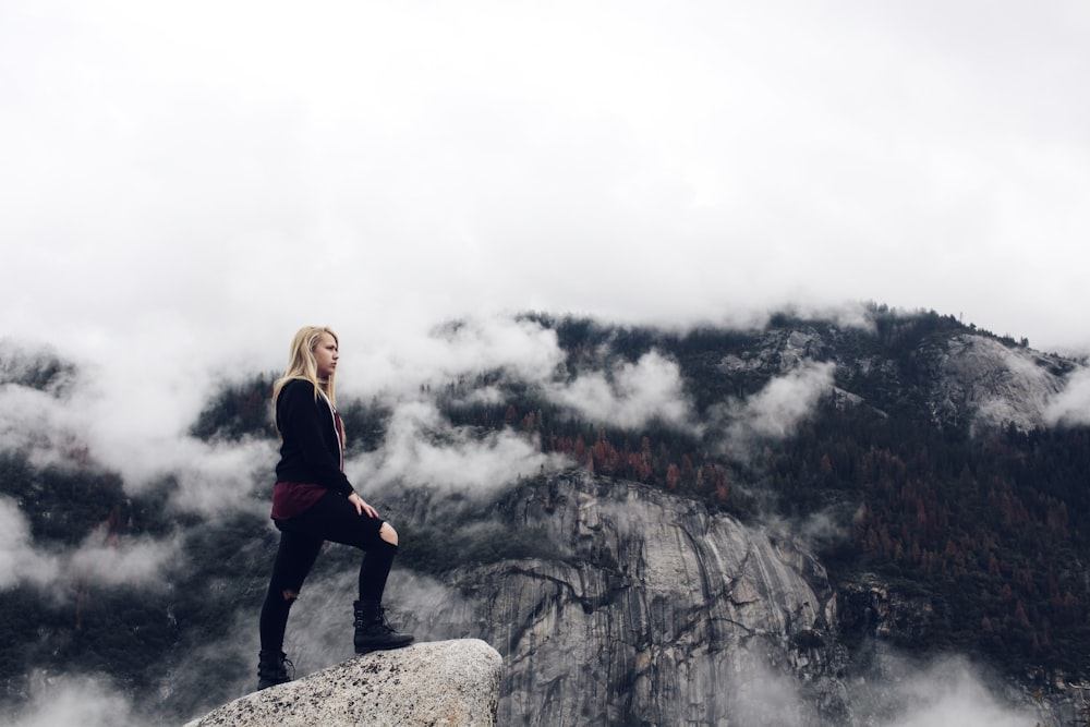 woman in black jacket standing on gray rock formation during daytime