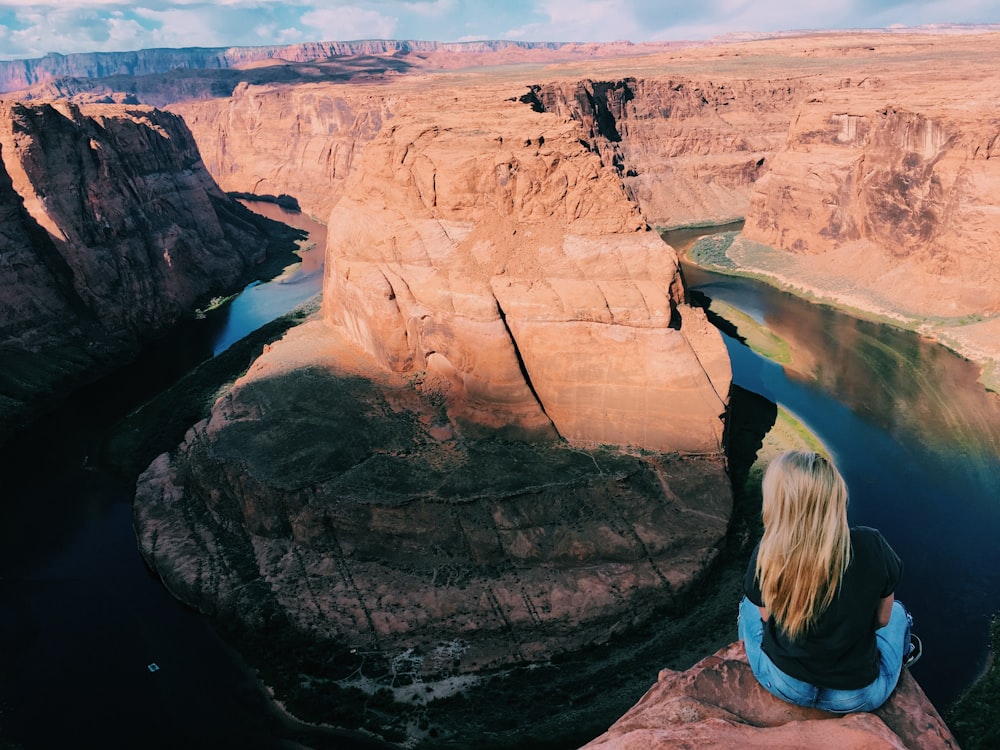 woman in blue denim jeans sitting on rock formation during daytime