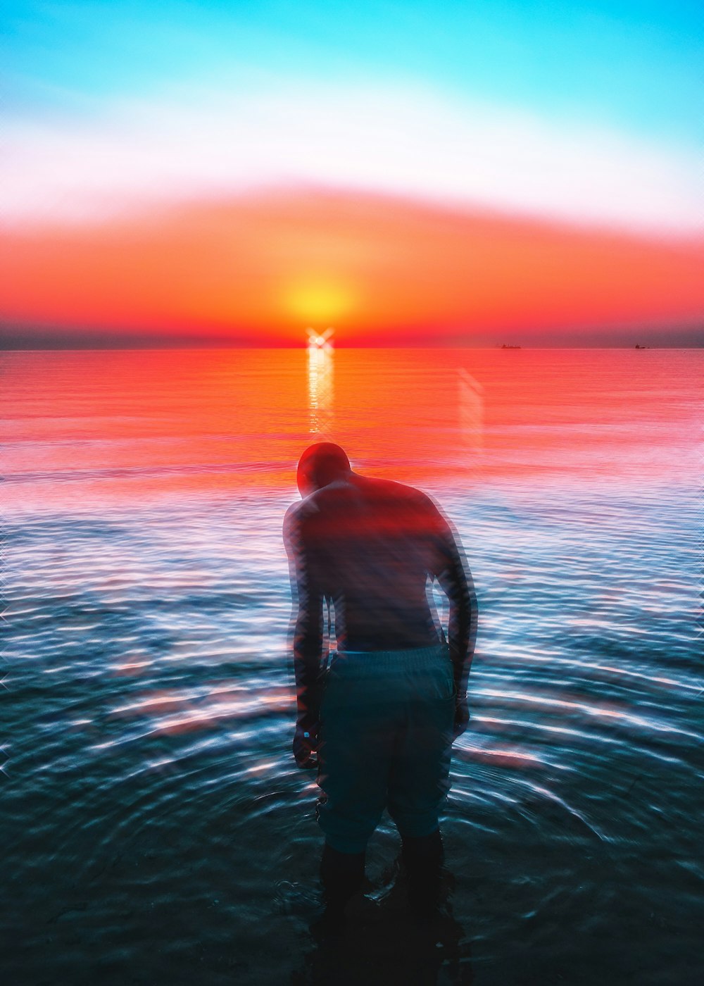 Hombre en camiseta sin mangas negra de pie en el agua durante la puesta del sol