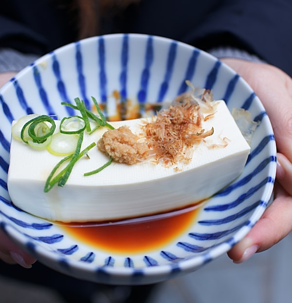 person holding white and blue ceramic plate with rice and sliced cucumber