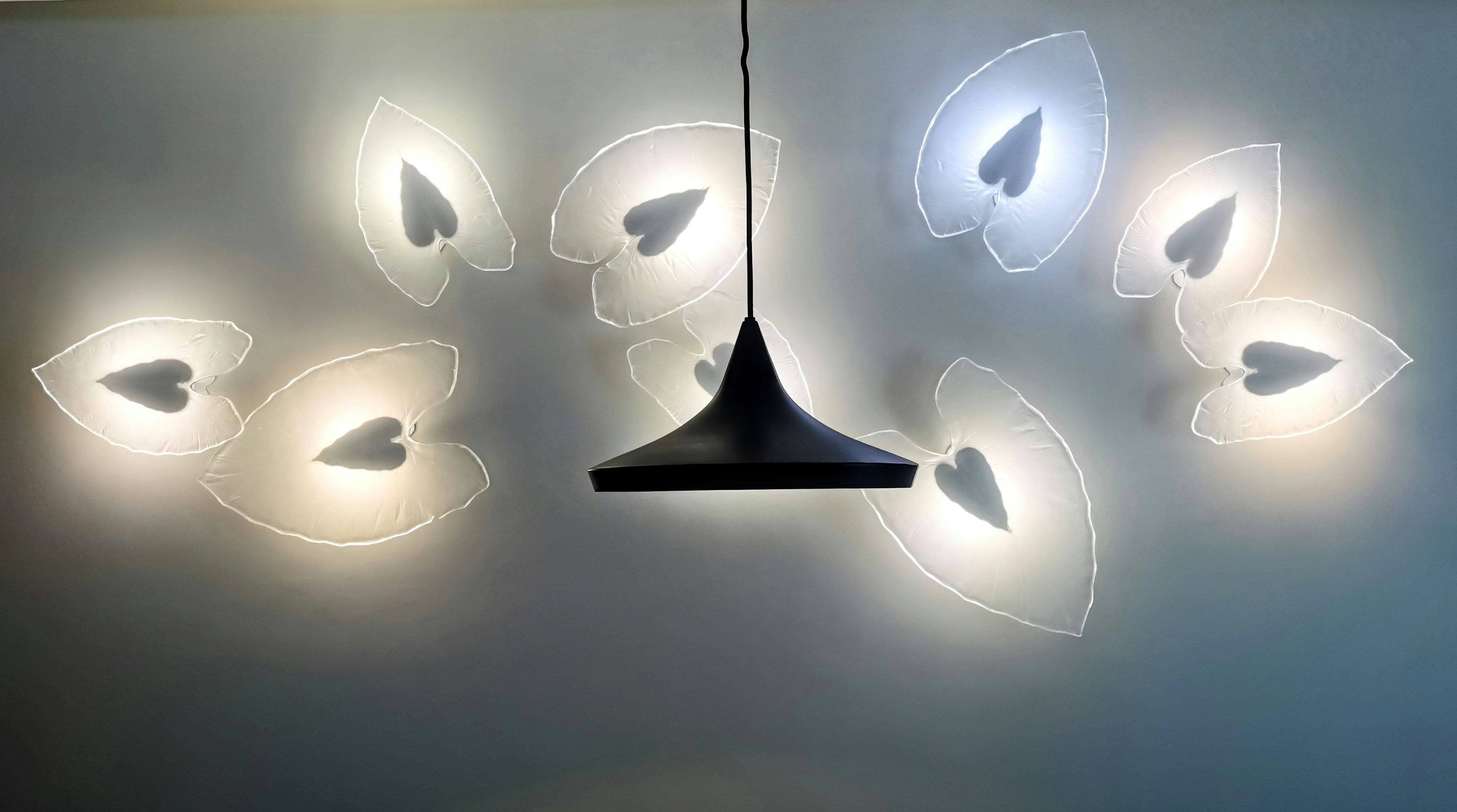 A modern light fixture on the ceiling features a series of illuminated leaf-shaped designs with heart-like cutouts, arranged in a symmetrical pattern around a central, dark, conical hanging light.