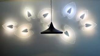 A modern light fixture on the ceiling features a series of illuminated leaf-shaped designs with heart-like cutouts, arranged in a symmetrical pattern around a central, dark, conical hanging light.