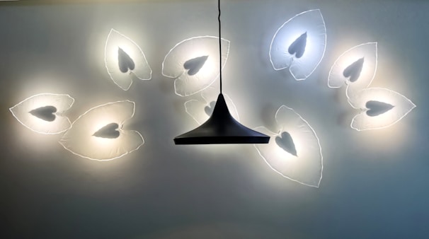 A modern light fixture on the ceiling features a series of illuminated leaf-shaped designs with heart-like cutouts, arranged in a symmetrical pattern around a central, dark, conical hanging light.