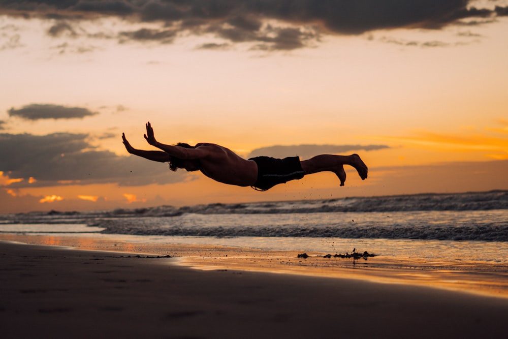 man in black shorts jumping on beach during sunset