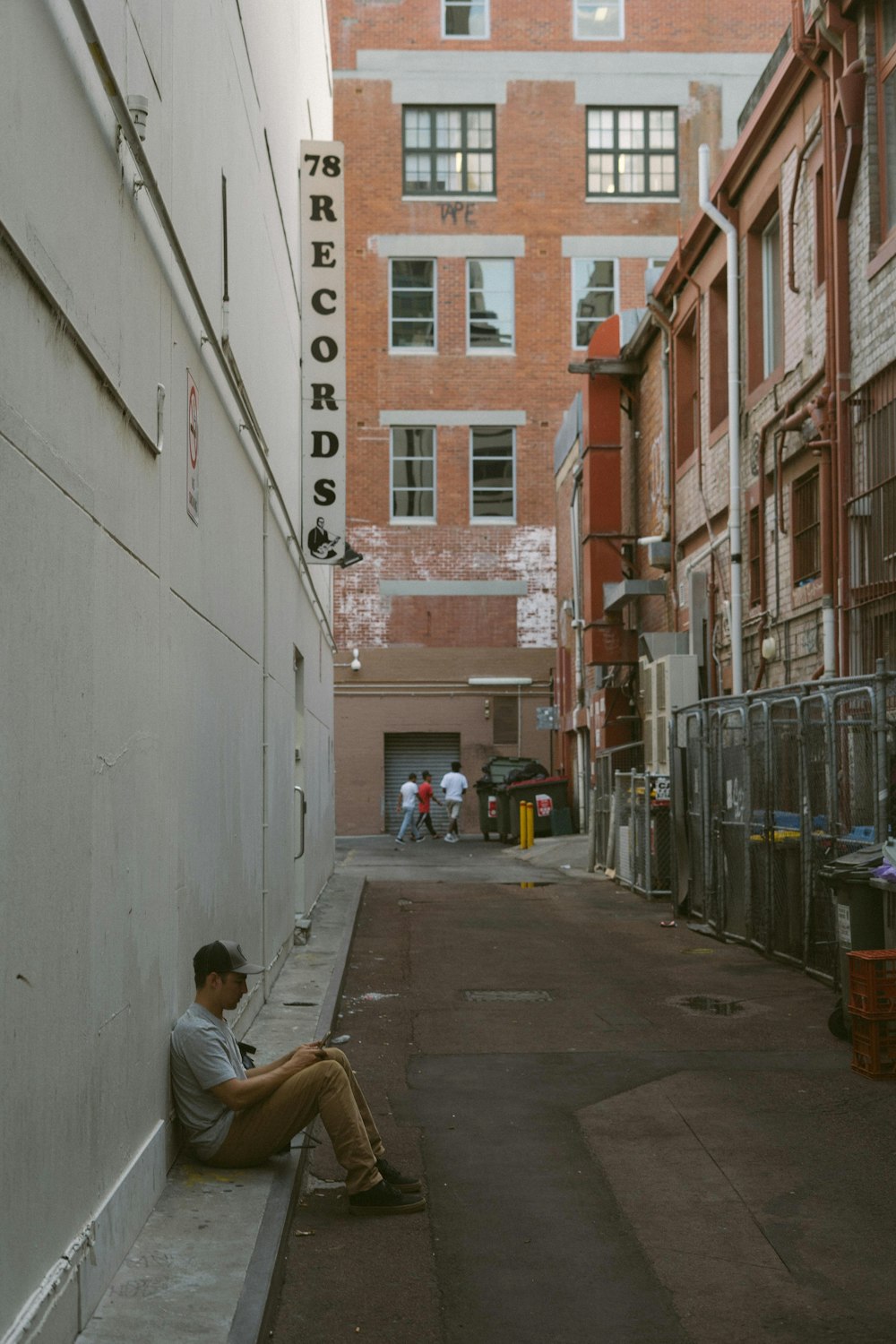 man in black jacket sitting on brown wooden bench near white concrete building during daytime