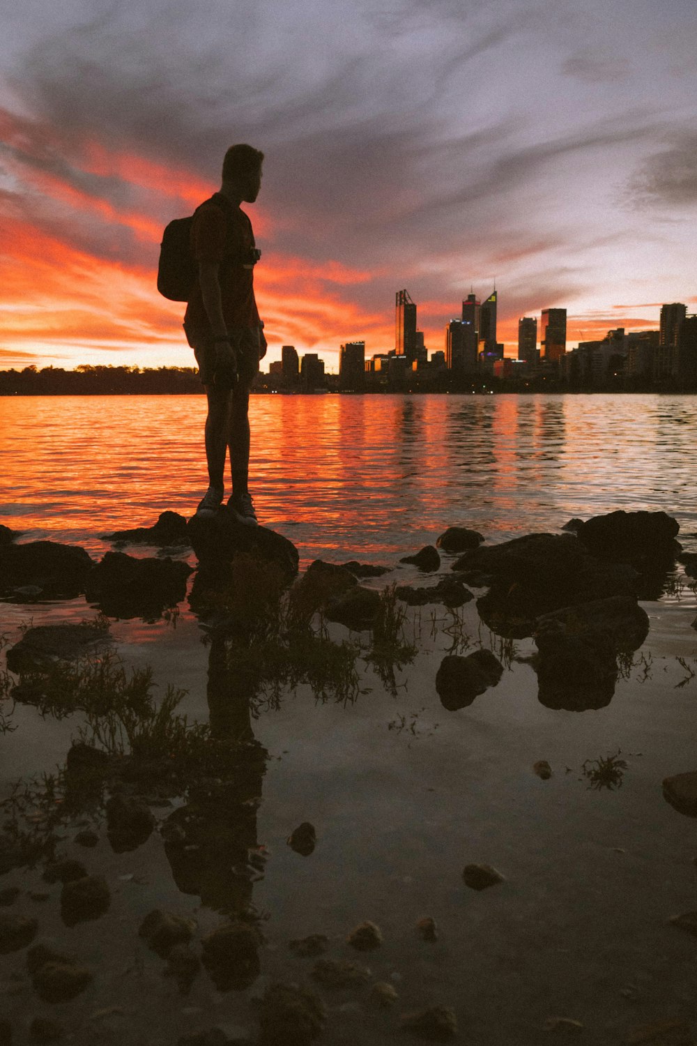 silhouette of man standing on rock near body of water during sunset