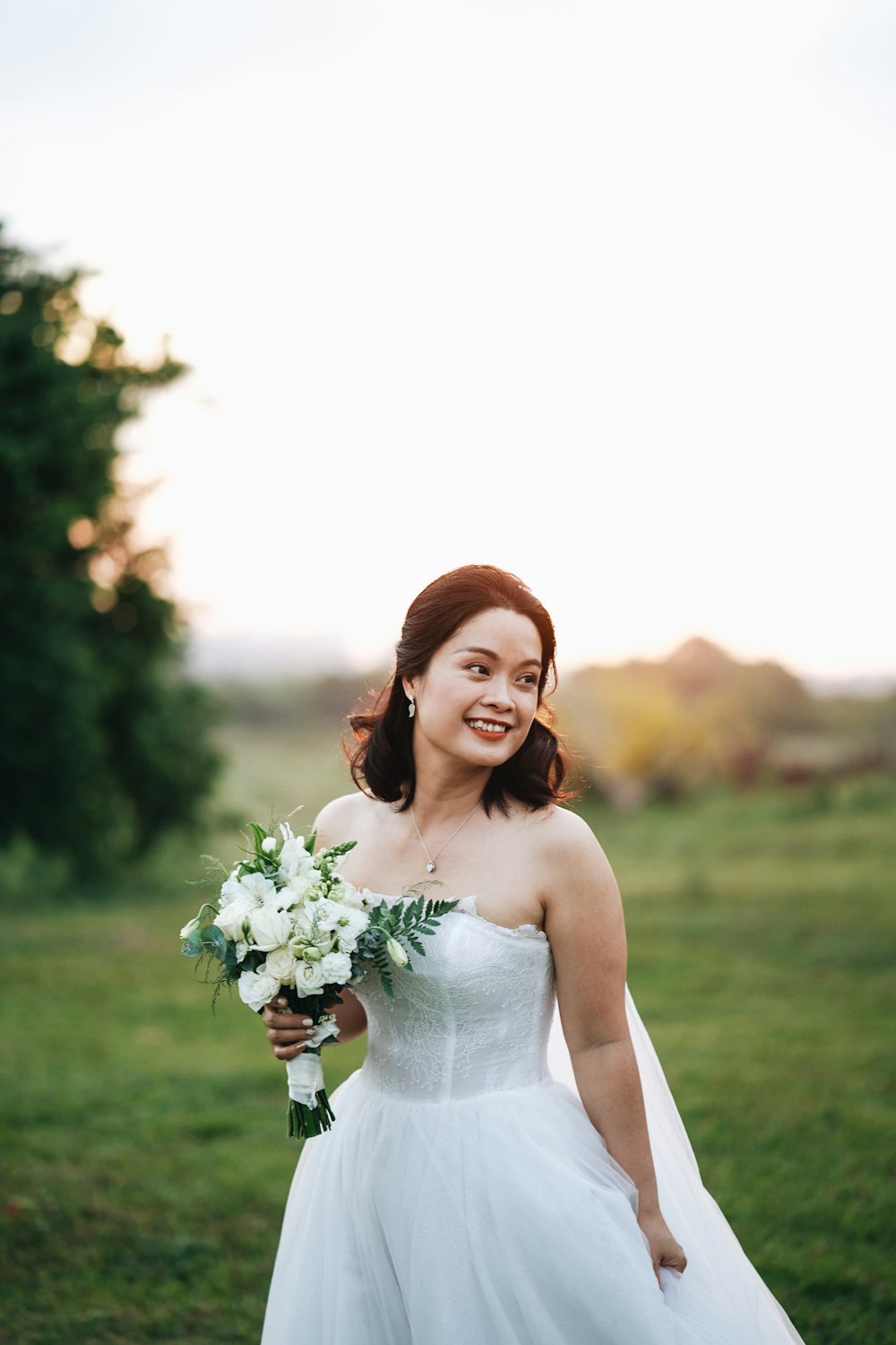 Mujer en vestido blanco de tirantes finos sosteniendo ramo de flores blancas