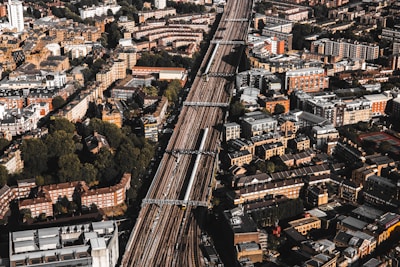 Aerial view of a densely populated urban area with a prominent railway line running through the center. The cityscape features a mix of residential and commercial buildings, mostly characterized by brick and stone facades. Green spaces are interspersed among the structures, providing a contrast to the urban density.