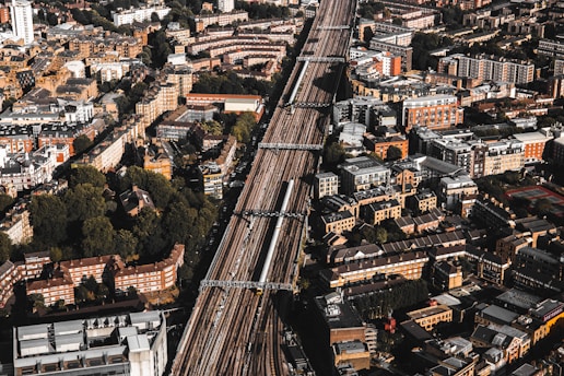 Aerial view of a densely populated urban area with a prominent railway line running through the center. The cityscape features a mix of residential and commercial buildings, mostly characterized by brick and stone facades. Green spaces are interspersed among the structures, providing a contrast to the urban density.