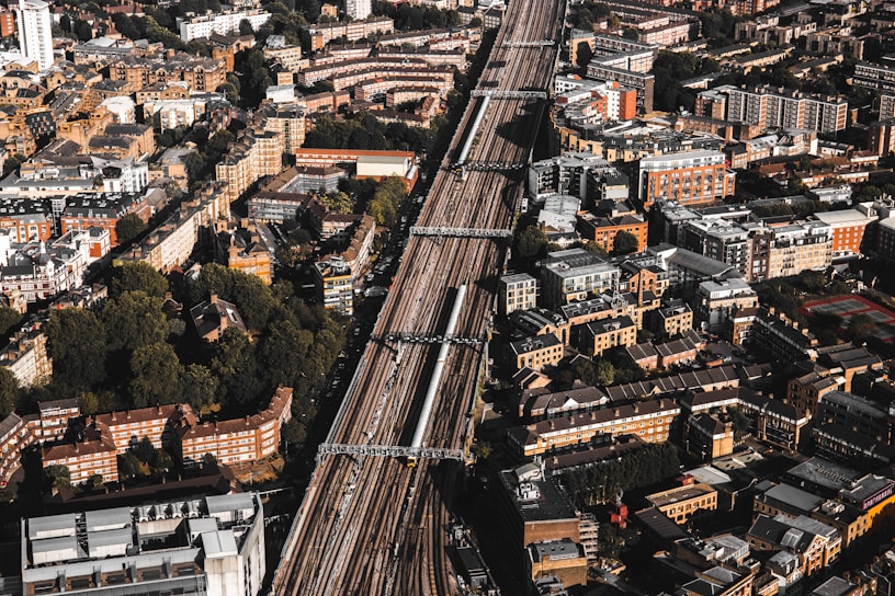 Aerial view of a densely populated urban area with a prominent railway line running through the center. The cityscape features a mix of residential and commercial buildings, mostly characterized by brick and stone facades. Green spaces are interspersed among the structures, providing a contrast to the urban density.