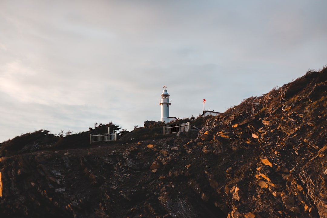 white and black lighthouse on brown rocky mountain under white cloudy sky during daytime