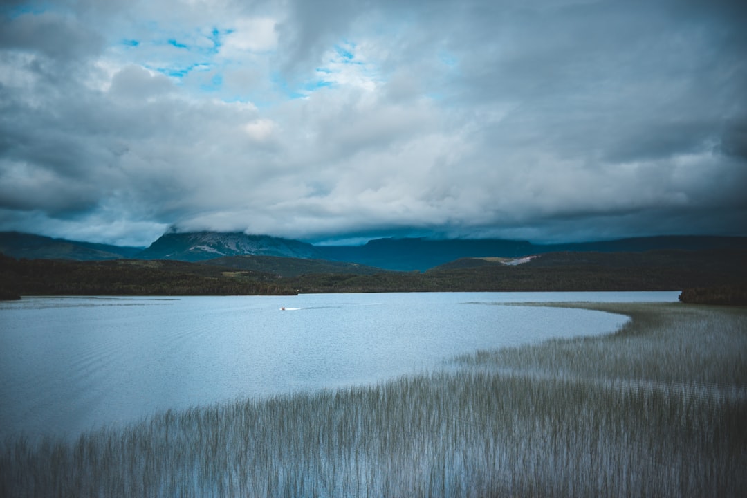 body of water near mountain under cloudy sky during daytime