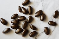 Several dark brown, oval-shaped seeds are scattered over a light marble surface, each seed has a smooth and shiny texture.