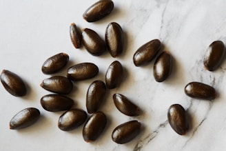 Several dark brown, oval-shaped seeds are scattered over a light marble surface, each seed has a smooth and shiny texture.