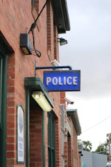 Exterior of a police station with faded signage and barred windows.