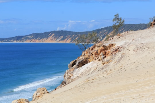 brown rocky mountain beside blue sea under blue sky during daytime in Rainbow Beach QLD Australia
