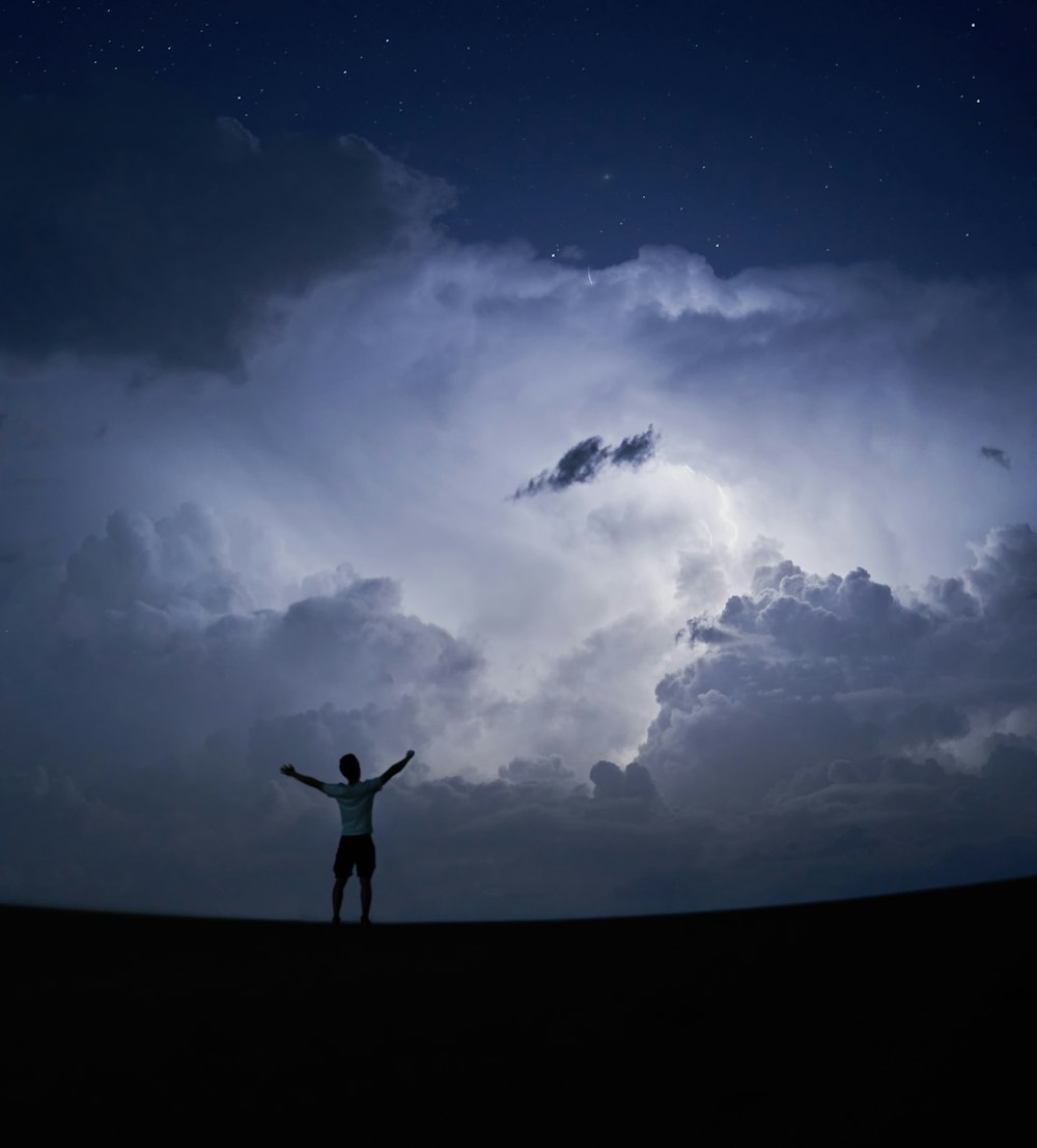 silhouette of person standing under blue sky and white clouds during daytime