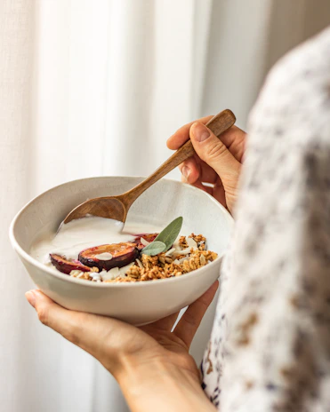 Smiling person enjoying a spoonful of granola outdoors surrounded by greenery.