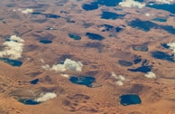A panoramic view of the vast Liwa desert with faint Arabic geometric patterns subtly overlaid on the sand.