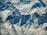 A stunning aerial view of rugged snow-covered mountains with sharp peaks and deep valleys, showcasing the massive, sheer cliffs and intricate patterns formed by the snow and ice.