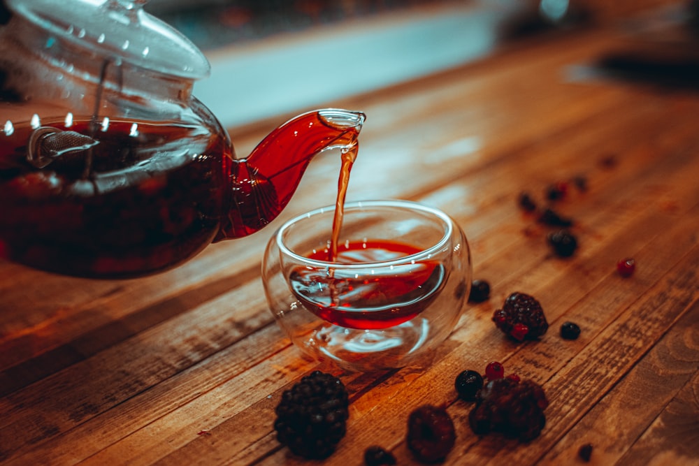 clear glass teapot with red liquid on brown wooden table