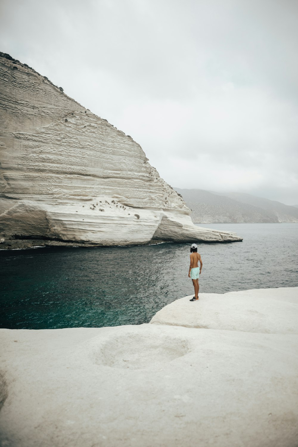 woman in blue denim shorts standing on rock formation near body of water during daytime