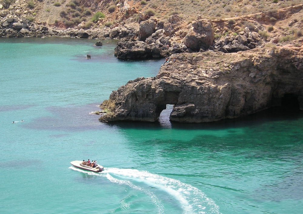 white and red boat on blue sea near brown rock formation during daytime