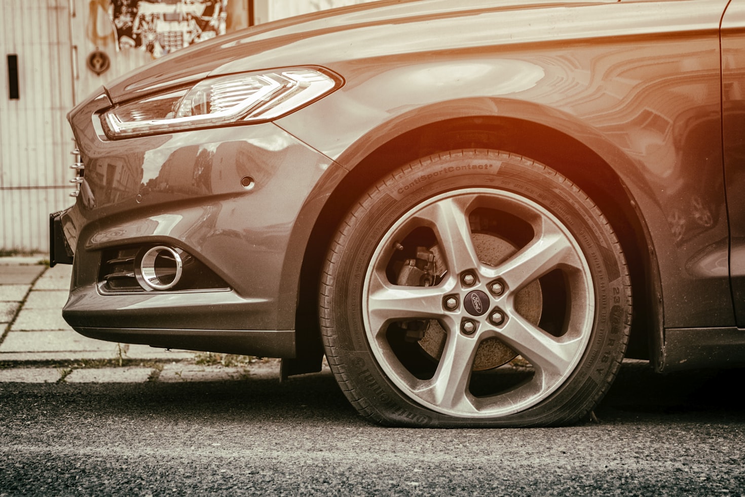 A car with a flat tire on the side of the road due to a car accident.