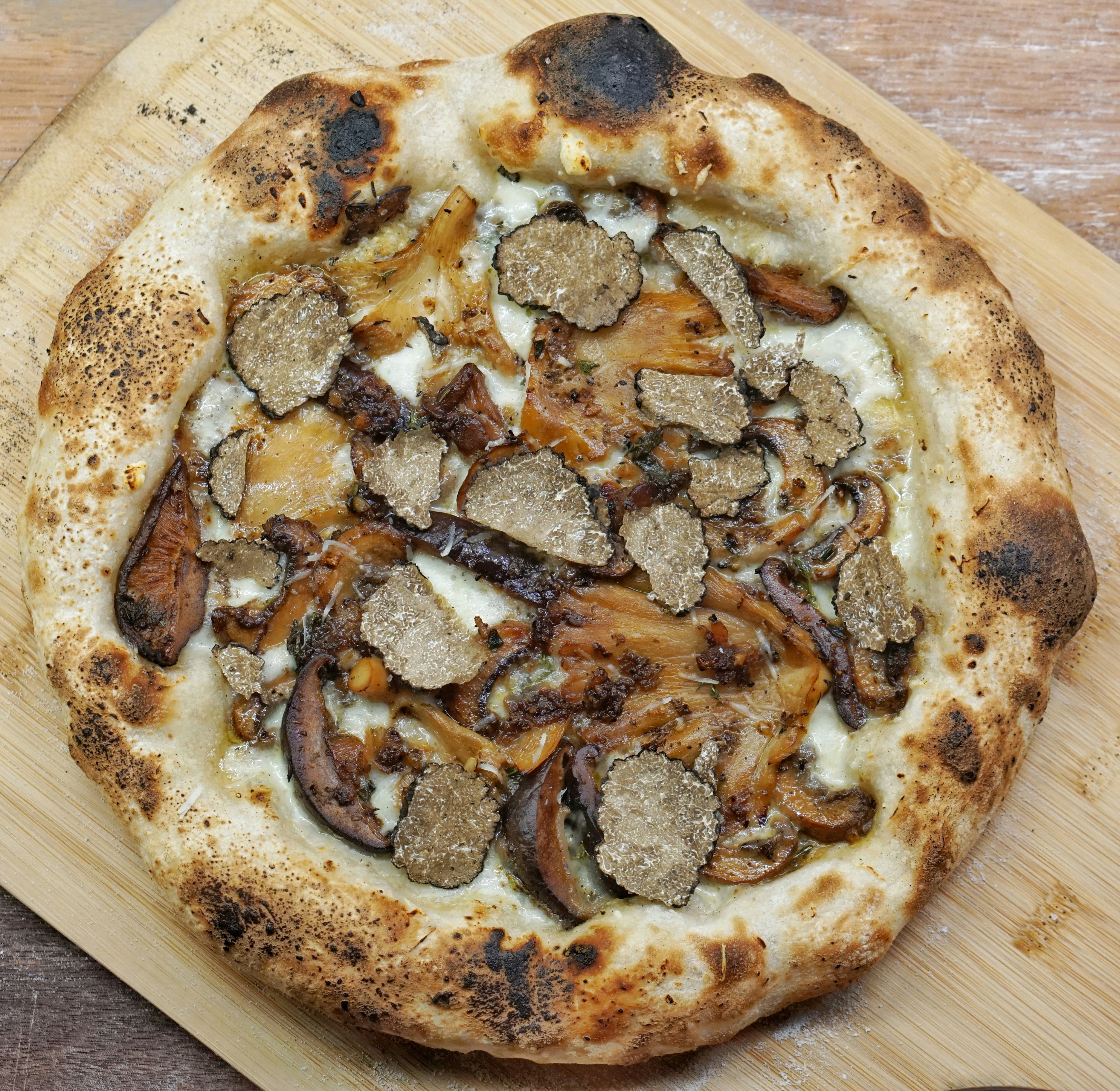 Gourmet truffle mushroom pizza on rustic wood board, dark atmospheric lighting, artisan toppings visible