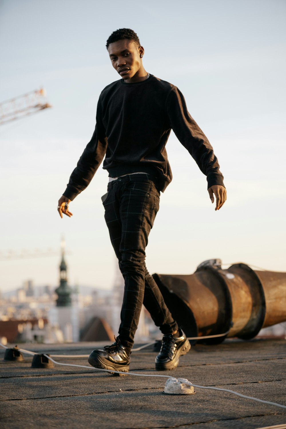 man in black long sleeve shirt and blue denim jeans standing on brown metal pipe during