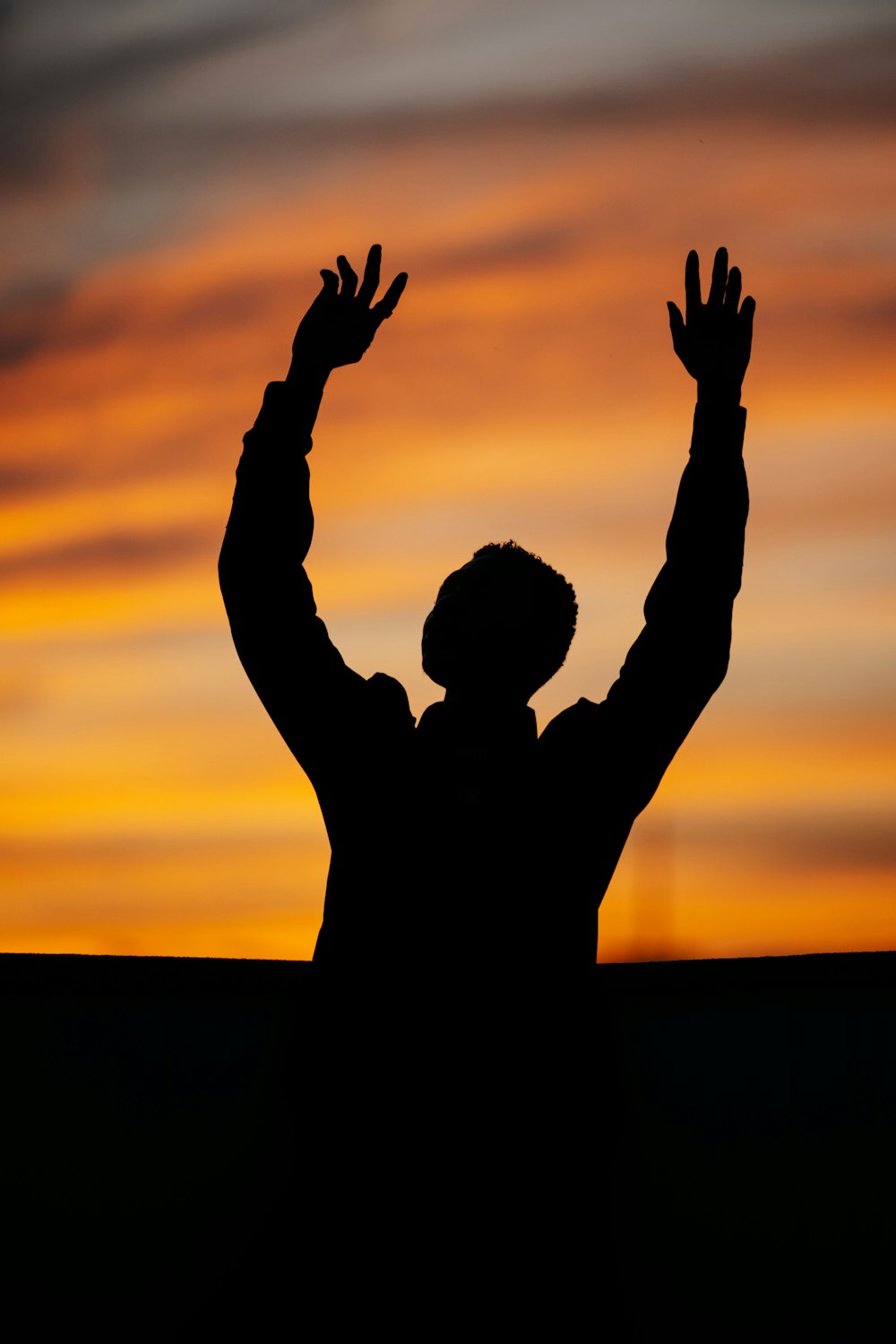 silhueta do homem levantando as mãos durante o pôr do sol