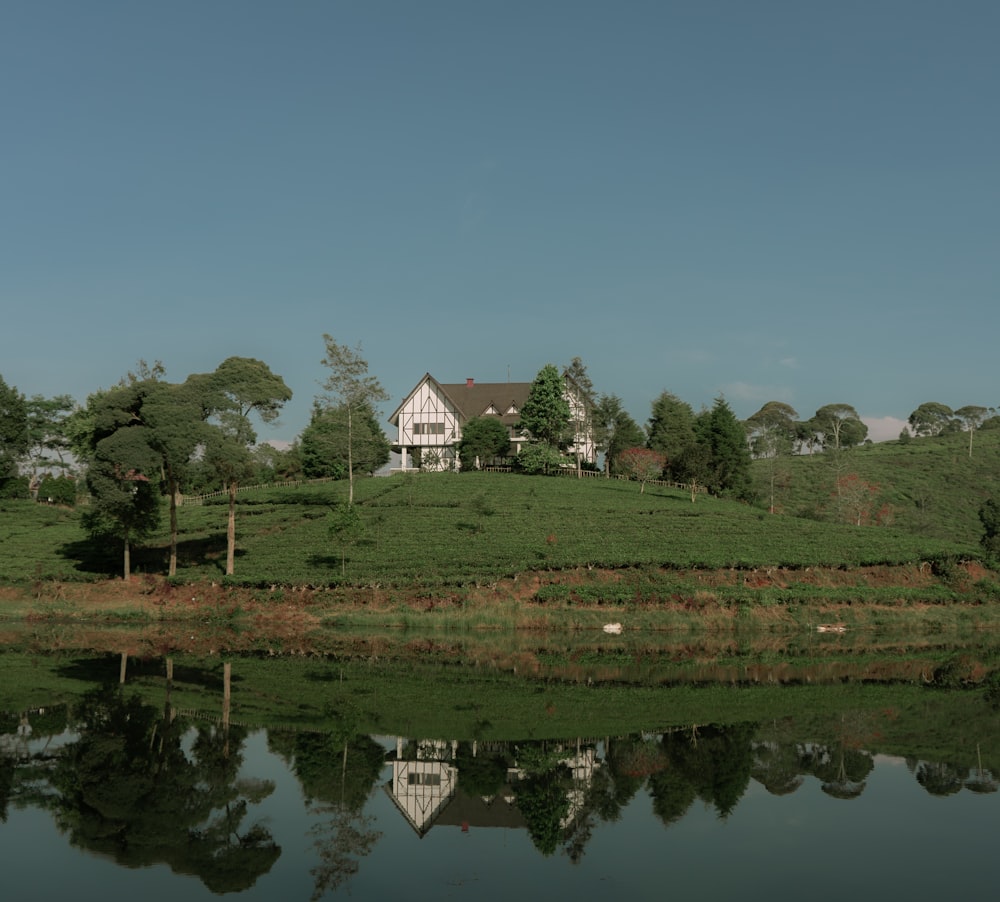 昼間は青空の下、緑の芝生と湖のそばにある白と茶色の家