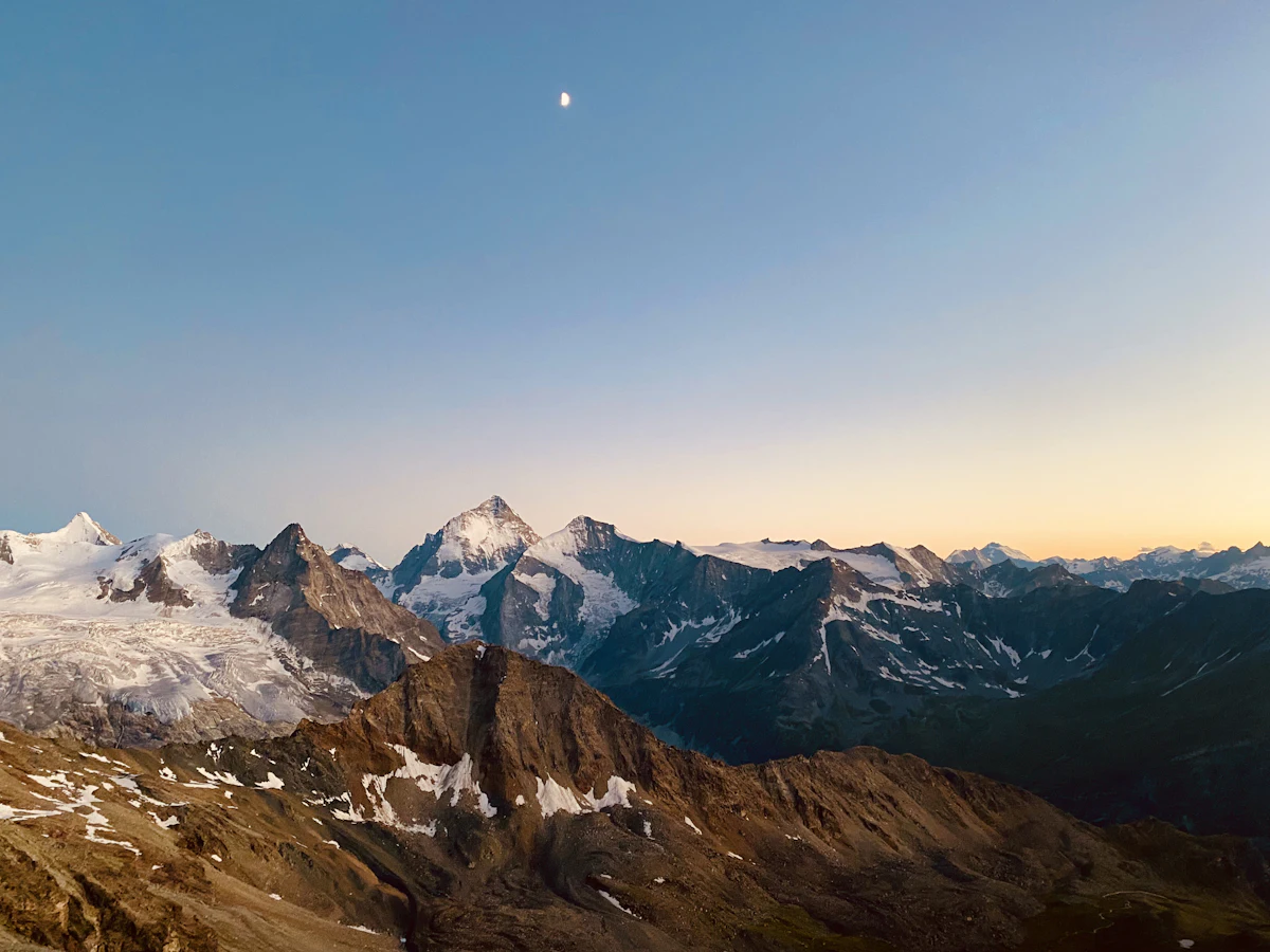 The moon over snowy peaks and glaciers at twilight, seen from near the Tracuit hut above Zinal