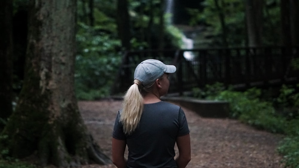 woman in black t-shirt and blue denim cap standing near green trees during daytime