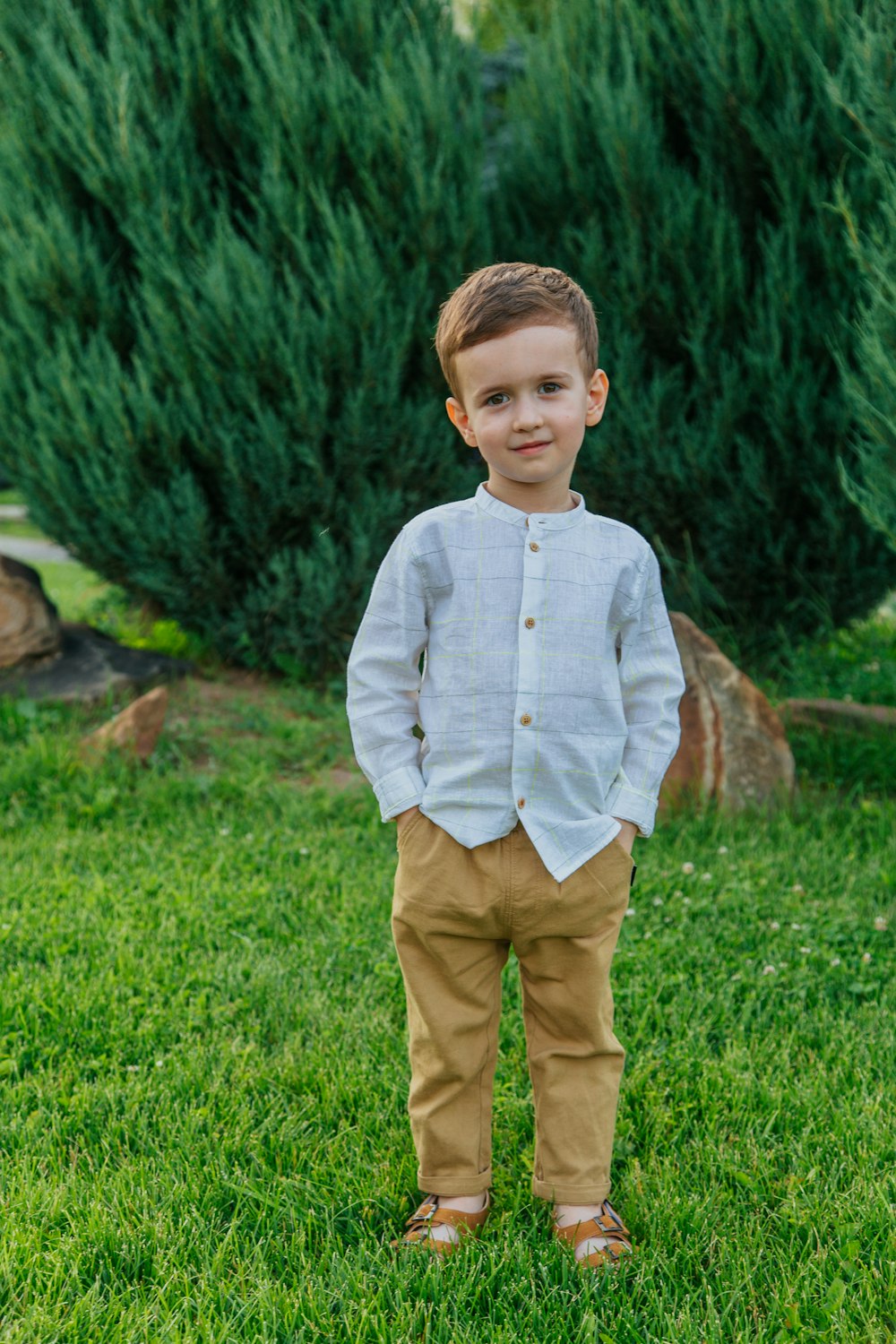 boy in blue dress shirt and brown pants standing on green grass field during daytime