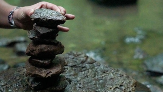 Close-up of hands gently holding natural stones stacked in a balanced cairn outdoors.