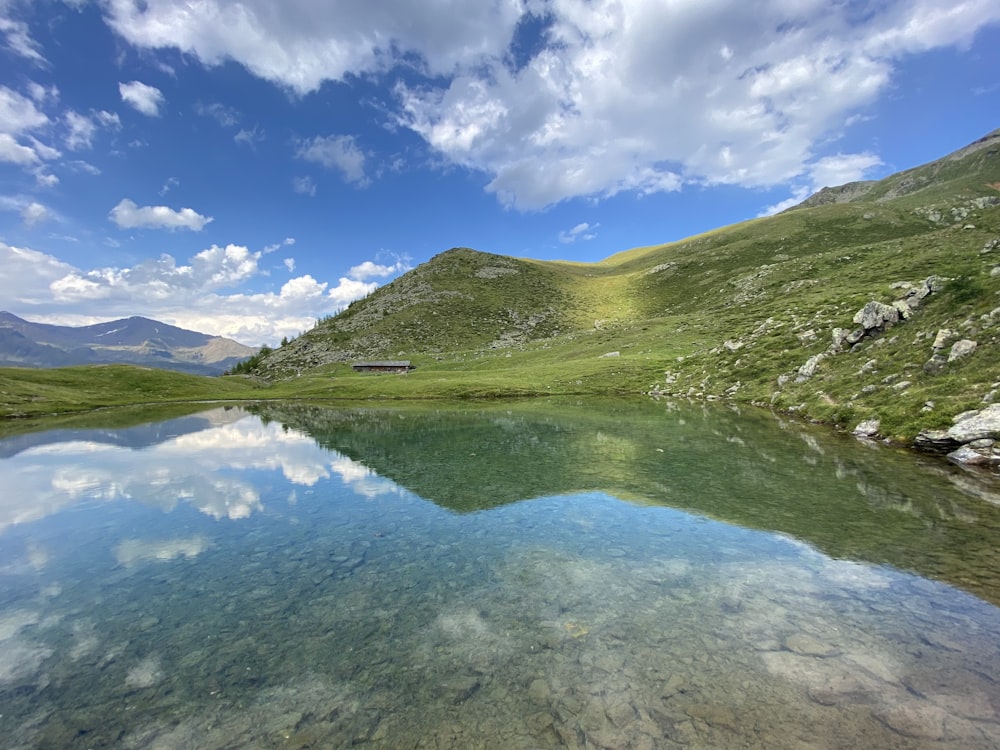 green grass covered mountain beside lake under blue sky during daytime