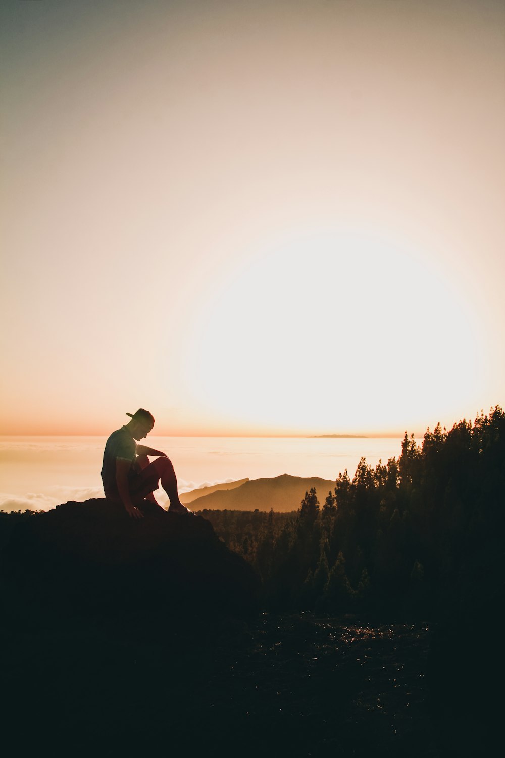 Silhouette eines Mannes, der bei Sonnenuntergang auf Felsen sitzt