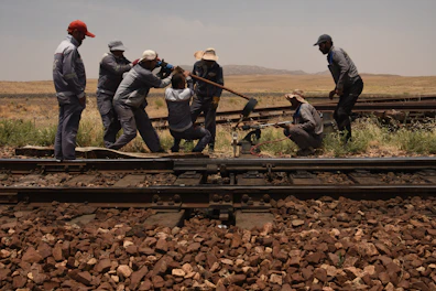 3 men in black jacket standing on train rail during daytime