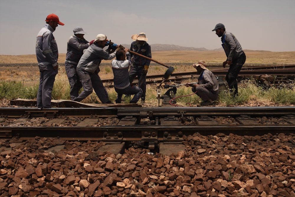 3 men in black jacket standing on train rail during daytime